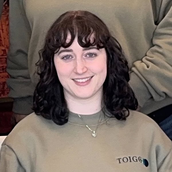 Toigo Foundation program participant, smiling woman in taupe sweatshirt with Toigo logo, promoting leadership development and diversity in finance and business.